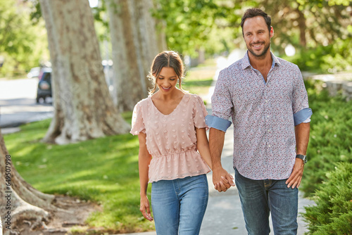 Smiling couple holding hands, walking on treelined sidewalk photo