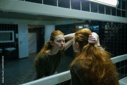 Young woman looking in mirror in public bathroom