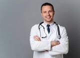 Healthcare, medical staff concept. Portrait of smiling male doctor posing with folded arms on grey studio background, free space. Professional general practitioner.