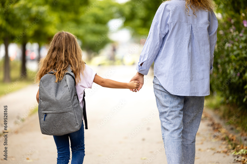 Mother and daughter holding hands together as walking towards the school.