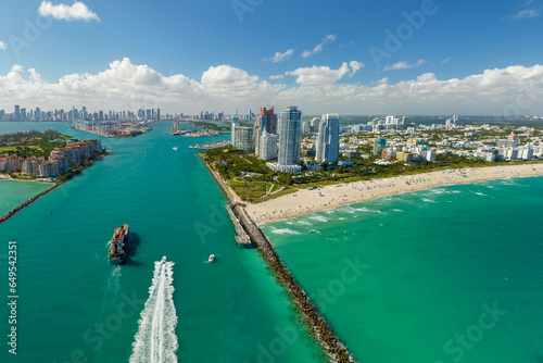 Aerial view of container ship entering in Miami harbor main channel near South Beach. Luxurious hotels and apartment buildings on waterfront and high skyscrapers of downtown district in distance © bilanol