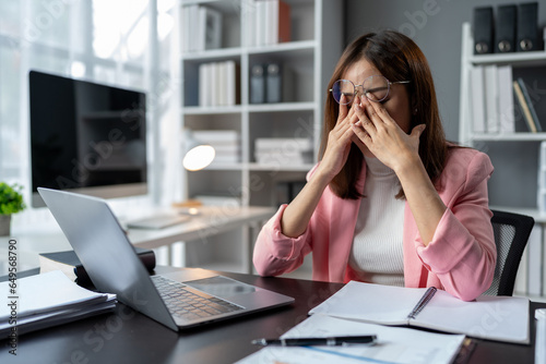 Stressed, tired, sleepy businesswoman bored from sitting at a desk for long hours and having office syndrome while working with laptop and financial paperwork. office marketing. photo