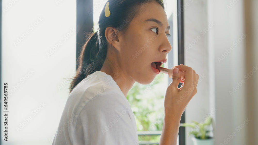 Young Asian happy woman make up looking at her reflection in mirror apply lip balm on her lips in bathroom. Lifestyle and people, Lips Protection, Natural Skin Care Cosmetics, Morning routine concept. Young Asian happy woman make up looking at her reflection in mirror apply lip balm on her lips in bathroom. Lifestyle and people, Lips Protection, Natural Skin Care Cosmetics, Morning routine concept.
