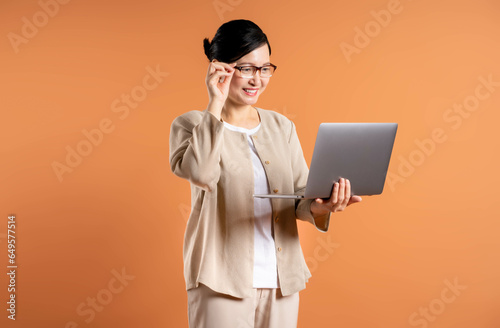 Portrait of middle age Asian woman using laptop on brown background.