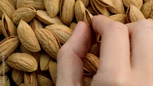 4K footage, top view of almonds in shell, a woman's hand with natural nails carefully takes one of the nuts. Calm scene, smooth movements. Raw fresh nuts