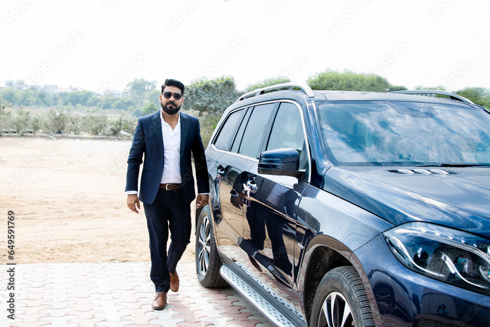 Handsome successful rich indian businessman in formal wear and sunglasses walking next to his car. Handsome successful rich indian businessman in formal wear and sunglasses walking next to his car.