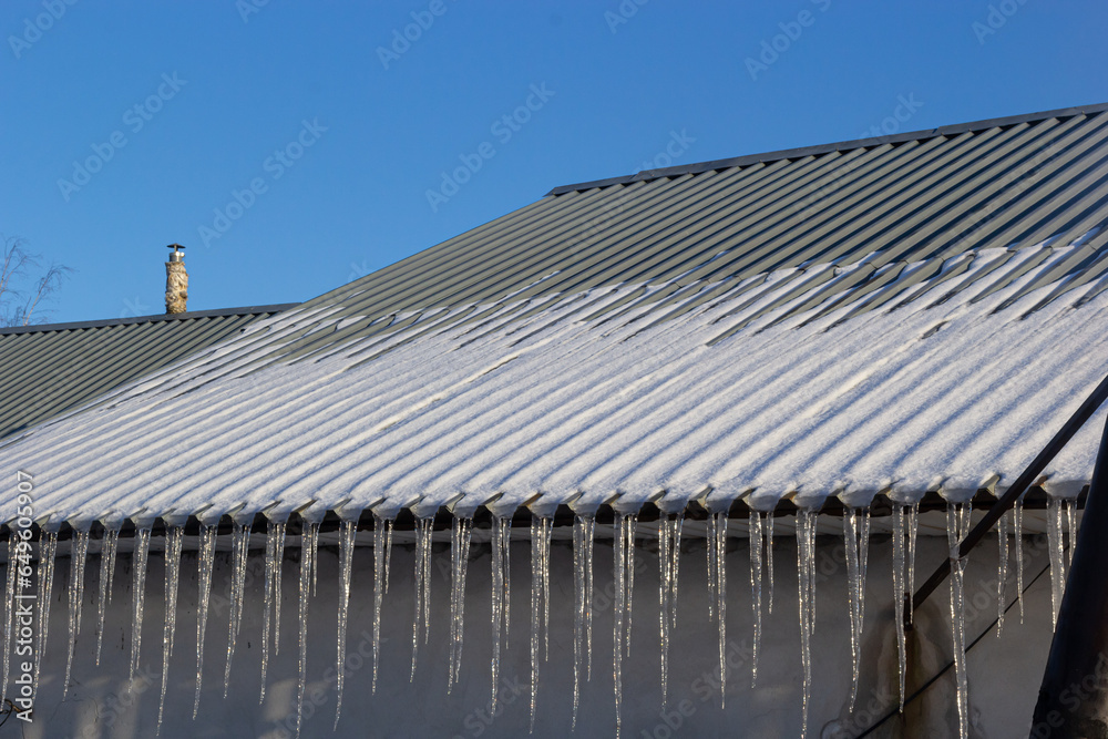 Sharp icicles and melted snow hanging from the eaves of the roof. Beautiful transparent icicles slowly gliding of a roof Sharp icicles and melted snow hanging from the eaves of the roof. Beautiful transparent icicles slowly gliding of a roof