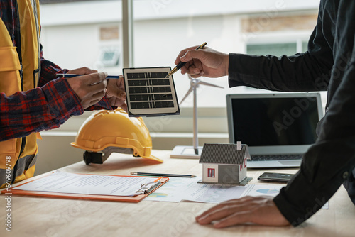 Fototapeta Naklejka Na Ścianę i Meble -  Two Caucasian engineers and architects work together in office with wind turbine and solar panels on table, renewable energy installation concept