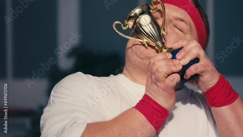 Excited overweight man celebrating success, kissing golden winner cup, smiling photo