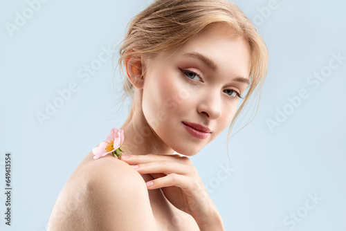 A mysterious young beautiful woman with natural makeup and glowing skin holds a rose flower and looks into the camera