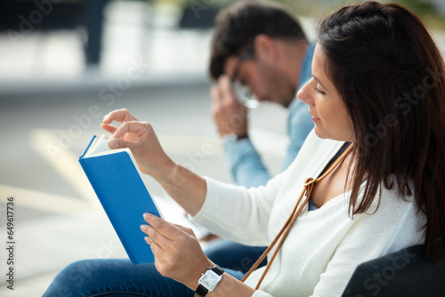 caucasian couple sitting at the train station woman reading book photo