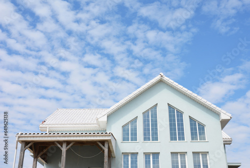 Exterior view of a triangular window design, irregular shape windows of the second level space, veranda, loft or attic of a light blue modern house with a white roof. © bildlove