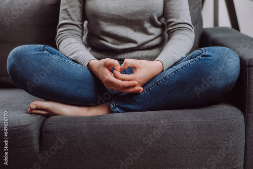 Unrecognizable young caucasian woman folded hands on knees together, sitting on sofa, unhappy female feeling lonely, suffering from domestic violence or relationship problem, break up with boyfriend