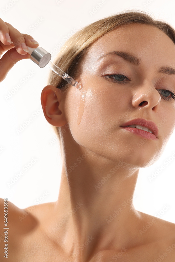 Beautiful woman applying cosmetic serum onto her face on white background