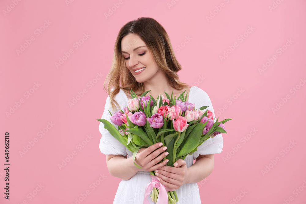 Happy young woman with bouquet of beautiful tulips on pink background