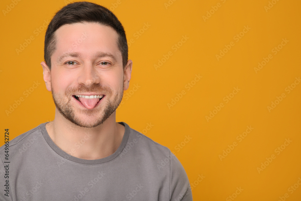 Obraz premium Happy man showing his tongue on orange background. Space for text