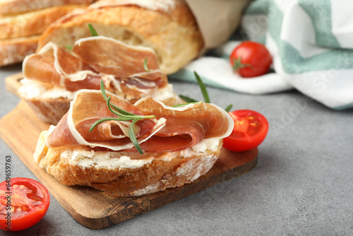 Tasty sandwiches with cured ham, tomatoes and rosemary on grey table, closeup