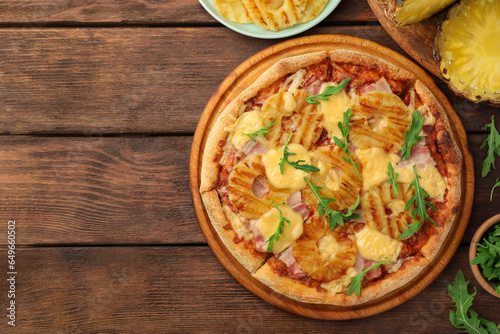 Delicious pineapple pizza and ingredients on wooden table, flat lay. Space for text