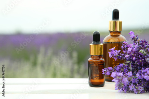 Bottles of essential oil and lavender flowers on white wooden table in field  space for text