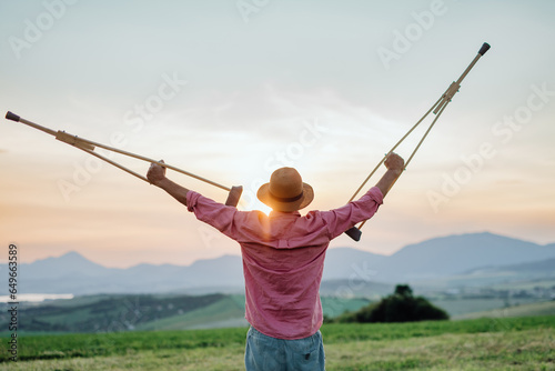 Rear view of senior man holding crutches in the air.