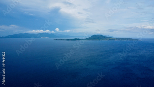 Uninhabited island in the Pacific Ocean and white clouds. Aerial view of a small uninhabited tropical island in a strait among the islands.