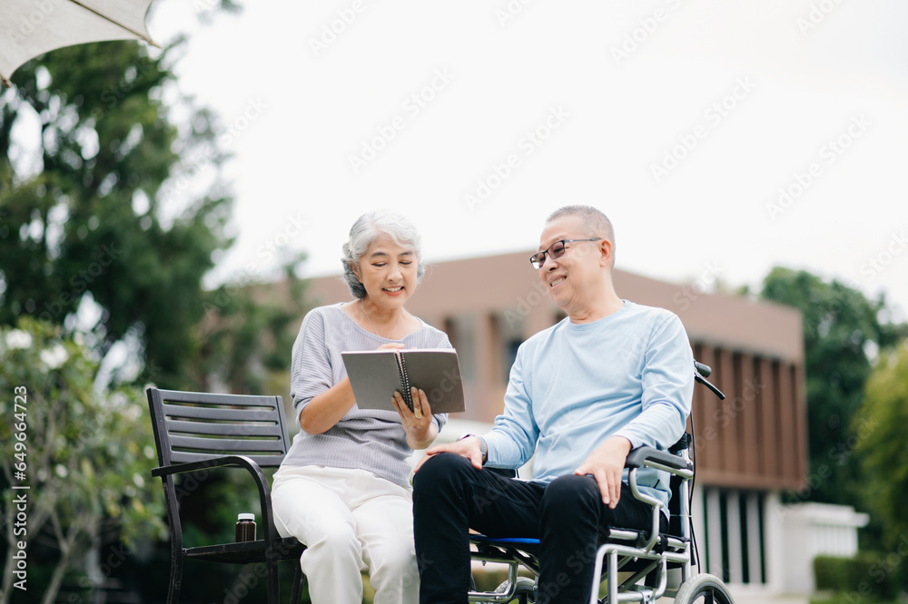 Asian Senior couple sitting in wheelchairs taking care of each other.in romantic time They laughing and smiling while sitting outdoor in park...