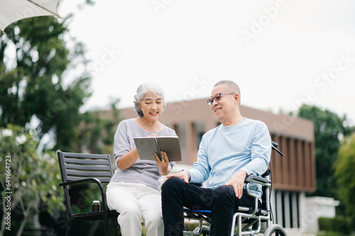 Asian Senior couple sitting in wheelchairs taking care of each other.in romantic time They laughing and smiling while sitting outdoor in park...