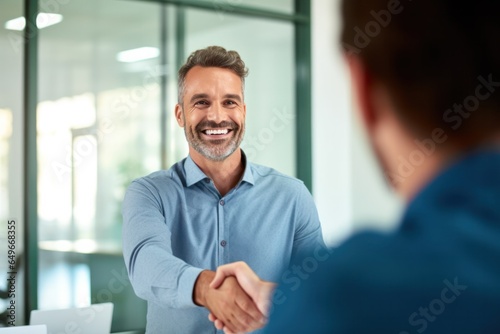 a smiling 40-year-old businessman shaking hands with his partner after signing an agreement during an office meeting