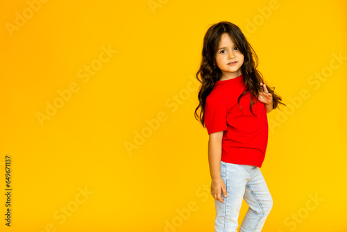 Little girl child cheerful little girl in jeans and a red T-shirt on a yellow background.