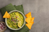 Bowl of delicious guacamole, nachos chips and lime on grey table, flat lay. Space for text