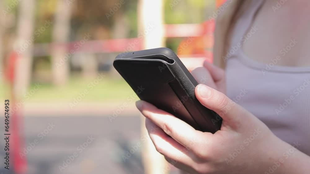 Female hands with a smartphone, close-up. Online communication, online shopping, social networks. A girl on an outdoor sports ground is looking for something on the Internet using her phone Female hands with a smartphone, close-up. Online communication, online shopping, social networks. A girl on an outdoor sports ground is looking for something on the Internet using her phone