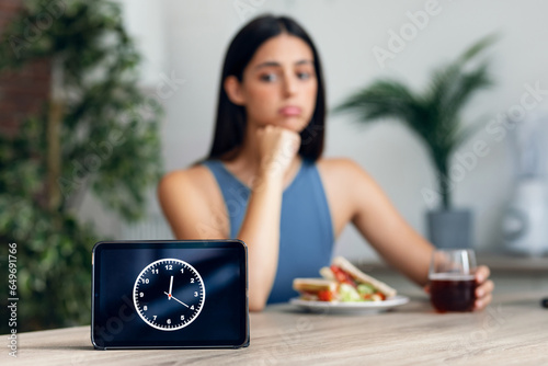 Hungry sporty woman waiting for the time to eat after fasting in the kitchen at home