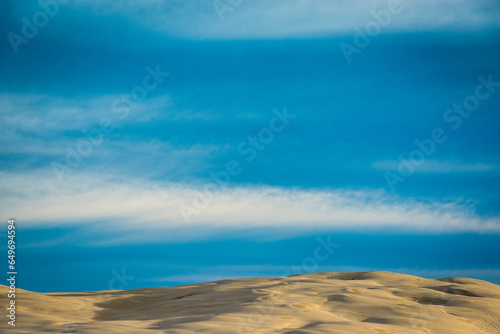 Sand dunes shot at sunrise in front of a blue sky with white clouds in the sky. There is a sense of isolation in the photo. 