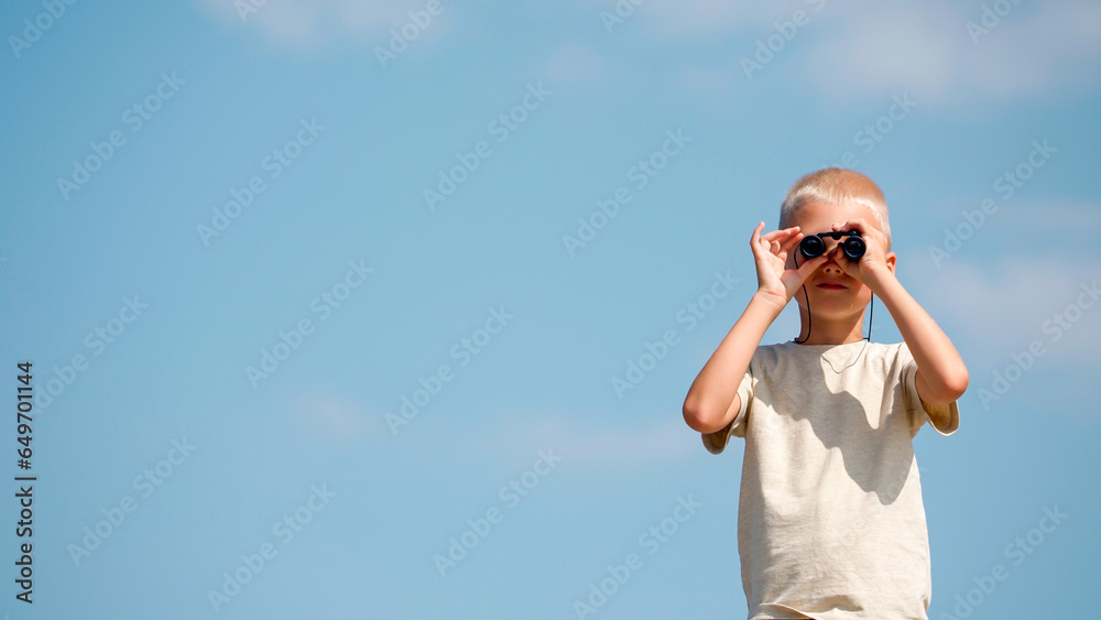 Portrait of a fair-haired European schoolboy looking through binoculars directly into the camera. An inquisitive child plays explorer or traveler, develops imagination. Active and healthy lifestyle. Portrait of a fair-haired European schoolboy looking through binoculars directly into the camera. An inquisitive child plays explorer or traveler, develops imagination. Active and healthy lifestyle.