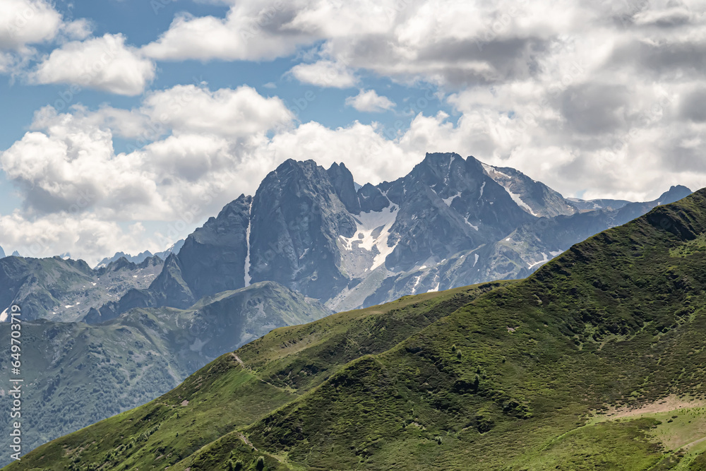 Fototapeta premium Mountain landscape with green slopes, cliffs, glaciers and white clouds in the sky