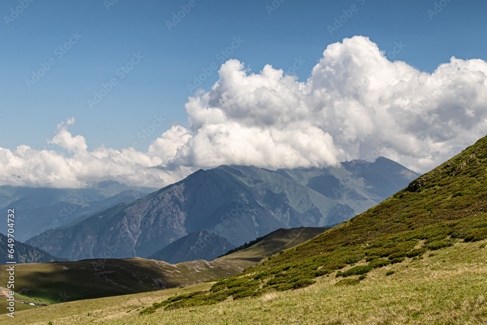 Mountain landscape with green slopes, cliffs, glaciers and white clouds in the sky