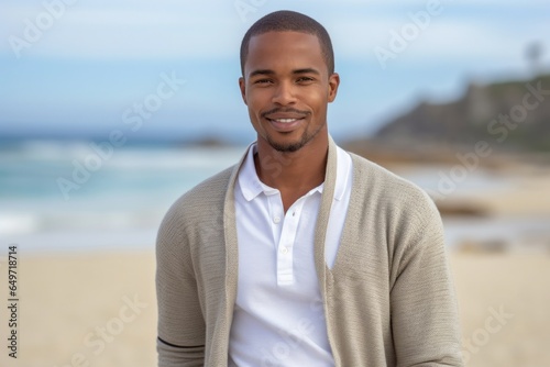 portrait of a confident Kenyan man in his 20s wearing a chic cardigan against a beach background