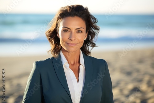 portrait of a confident Mexican woman in her 50s wearing a sleek suit against a beach background © Robert MEYNER