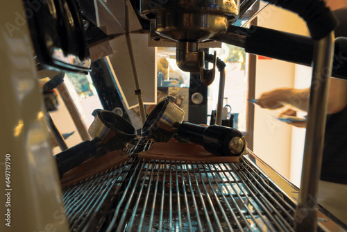 Close-up shot of a small cafe's espresso machine in the early morning from behind the bar hile a barista, a skilled artisan, works in the background. The coffee machine stands as the focal point photo