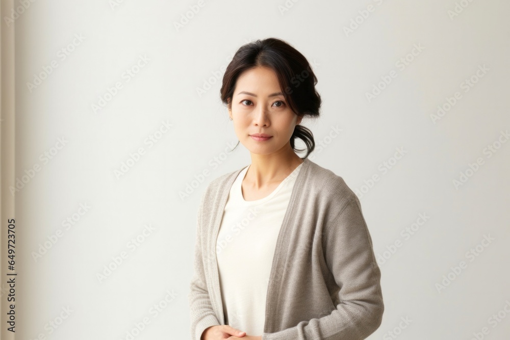 medium shot portrait of a serious, Japanese woman in her 40s wearing a chic cardigan against a minimalist or empty room background medium shot portrait of a serious, Japanese woman in her 40s wearing a chic cardigan against a minimalist or empty room background