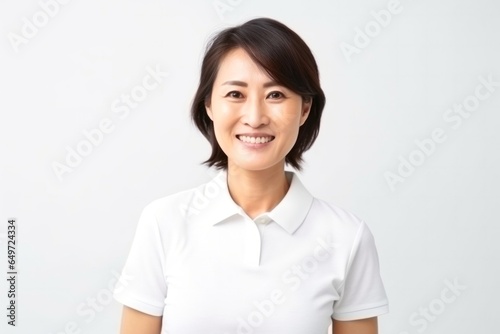 medium shot portrait of a happy Japanese woman in her 40s wearing a sporty polo shirt against a minimalist or empty room background © Anne-Marie Albrecht