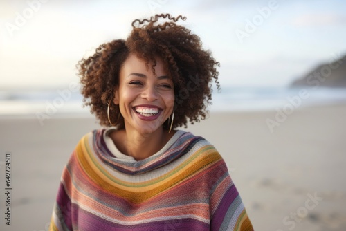 medium shot portrait of a happy Kenyan woman in her 30s wearing a cozy sweater against a beach background