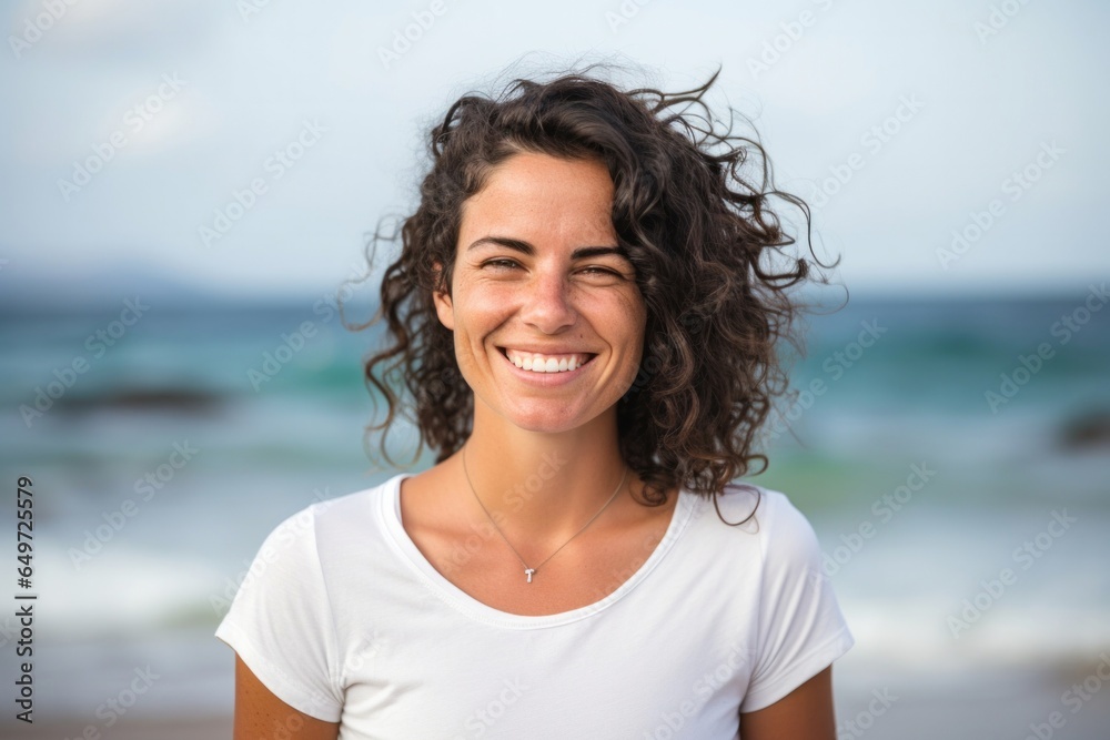 medium shot portrait of a happy Israeli woman in her 30s wearing a casual t-shirt against a beach background - obrazy, fototapety, plakaty 