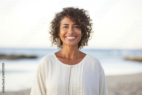 medium shot portrait of a happy Mexican woman in her 50s wearing a simple tunic against a beach background