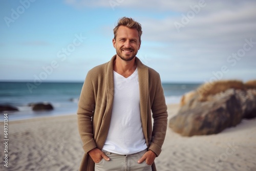 medium shot portrait of a Polish man in his 30s wearing a chic cardigan against a beach background