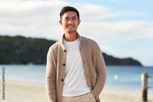 medium shot portrait of a confident Filipino man in his 30s wearing a chic cardigan against a beach background