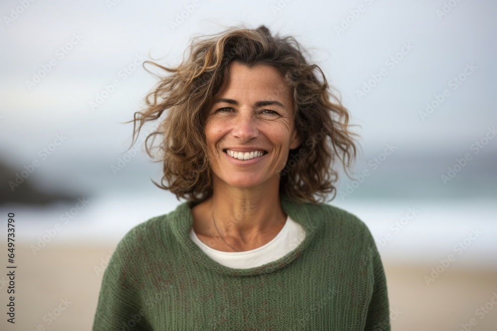 medium shot portrait of a confident Israeli woman in her 50s wearing a cozy sweater against a beach background