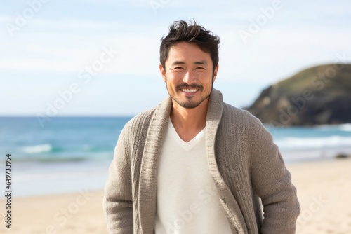 medium shot portrait of a confident Japanese man in his 30s wearing a chic cardigan against a beach background