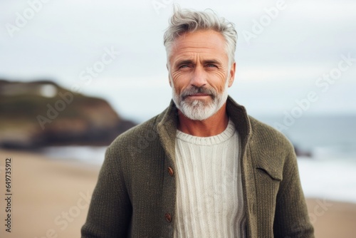 portrait of a Polish man in his 50s wearing a chic cardigan against a beach background
