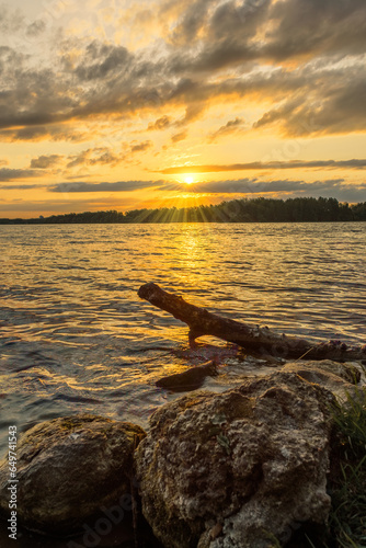 Stones and a snag on the background of the lake and sunset in summer